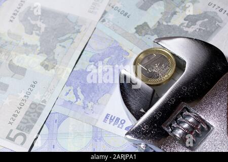 Eine Euro-Münze in einem verstellbaren Schraubenschlüssel auf verschiedenen Euro-Banknoten. Stockfoto