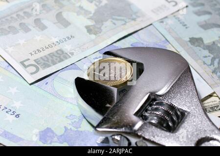 Eine Euro-Münze in einem verstellbaren Schraubenschlüssel auf verschiedenen Euro-Banknoten. Stockfoto