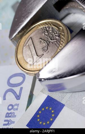 Eine Euro-Münze in einem verstellbaren Schraubenschlüssel auf verschiedenen Euro-Banknoten. Stockfoto