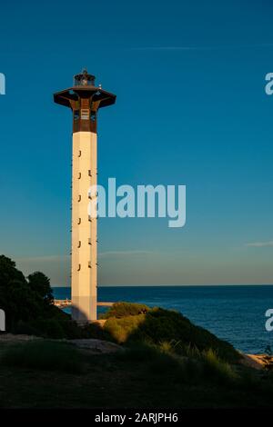 Der Leuchtturm Torredembarra ist eine markante weiße und holzige Struktur gegen einen tiefblauen Himmel im goldenen Stundenlicht des Mittelmeers. Stockfoto