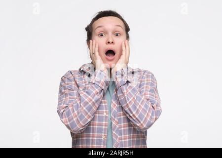 Junge Teenager schreien schockiert, haben vergessen, mit ihren Hausaufgaben fertig zu werden, und halten sich die Hände auf ihre Wangen. Studio gedreht Stockfoto