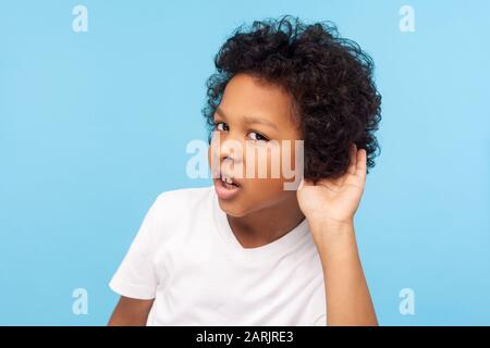 Was? Ich kann Sie nicht hören. Portrait des aufmerksamen neugierigen kleinen Jungen mit lockigem Haar, das die Hand in der Nähe des Ohrs hält und aufmerksam auf das hört, was Sie sagenhaft hören Stockfoto