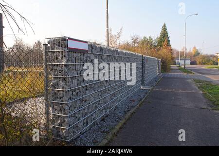 Wand, die das Haus von der Straße aus Gabionen trennt. Herbst. Stockfoto