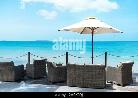 Ein Café im Freien mit Korbmöbeln und Sonnenschirmen auf türkisfarbenem Meeresgrund. Tropisches Urlaubskonzept. Stockfoto