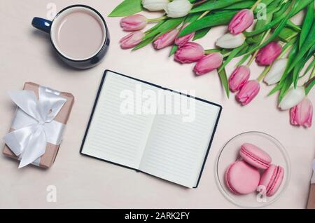 Frühstück auf dem Tisch. Flat Lay Komposition mit Blumen, Notizblock eine Tasse Kaffee und Süßigkeiten. Konzept Hallo Frühling Stockfoto
