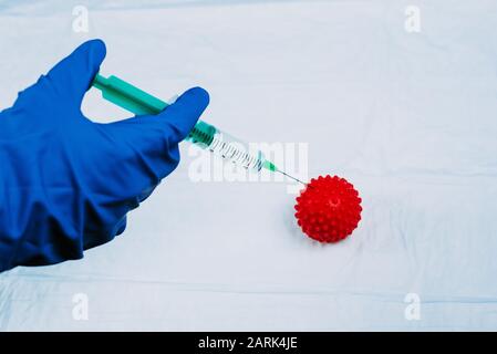 Ein Arzt in einem blauen Kunststoffhandschuh wirft eine Spritze in eine rote Kugel aus Coronavirus auf Kunststofffolie ein. Behandlung einer chinesischen Infektion. Flaches Layout, Copyspace. Stockfoto