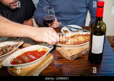 Nahaufnahme von zwei Männern, die zusammen mit einer Flasche Wein eine Mahlzeit einnehmen Stockfoto