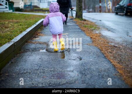 Ein kleines Mädchen, das Spaß hat, an einem regnerischen Tag in Pfützen zu planschen. Stockfoto