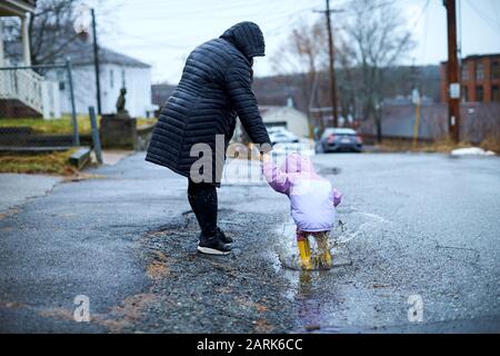 Eine Mutter und ein Kind, die Spaß haben, an einem regnerischen Tag in Pfützen zu planschen. Stockfoto