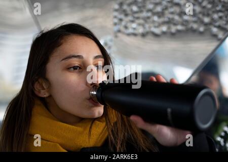 Junge Frau trinkt Wasser aus einem schwarzen Thermostat. Thermos-Konzept. Stockfoto