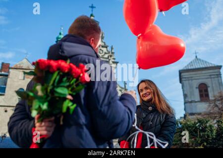 Valentinstag Rosen. Mann versteckt Blumenstrauß von Freundin hinter dem Rücken mit Luftballons. Damen Day Stockfoto