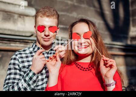 Valentinstag Fotostand Requisiten. Mann und Frau verstecken die Augen hinter roten Herzen. Paare haben Spaß Stockfoto