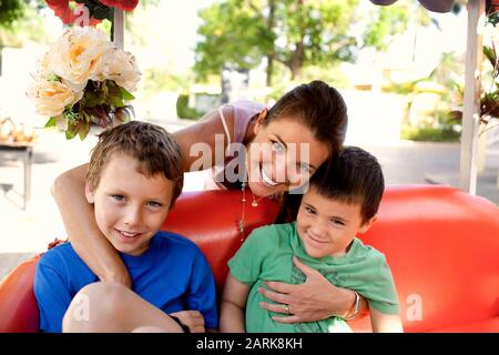 Lächelnde Frau und ihre beiden Söhne lächelten in einem Transportfahrzeug sitzen. Stockfoto