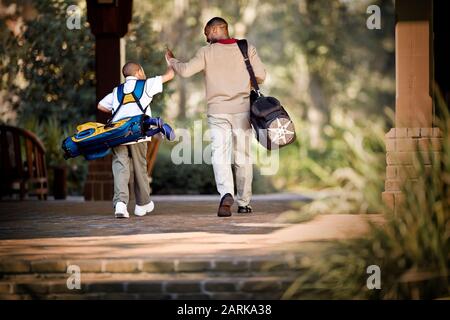 Vater und Sohn tragen Golfbeutel und hohes Fiving Stockfoto