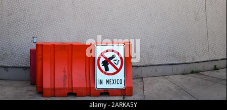 Ein Schild mit schwarz-weißer Clipkunst einer Handfeuerwaffe mit Kugeln, die von rotem Kreis mit Linie umgeben sind und vermitteln, dass keine Schusswaffen nach Mexiko dürfen Stockfoto