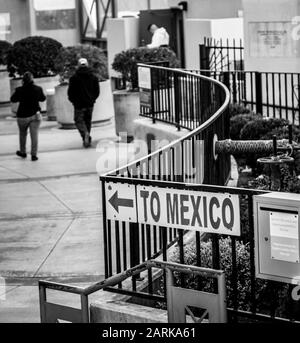 Ein Schild, das auf Mexiko zeigt, mit Rückblick auf Menschen, die an einem Einstiegscheck in Nogales, AZ, USA, schwarz-weiß in Richtung der US-mexikanischen Grenze gehen Stockfoto