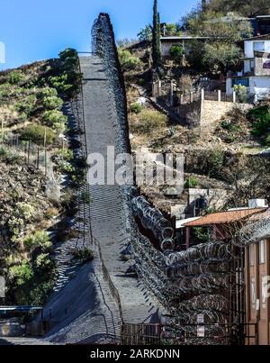 Blick auf den internationalen Grenzzaun aus US/Mexiko mit Rasierdraht, der sich bergauf mit mexikanischen Häusern auf der anderen Seite des Zauns von Nogales, AZ, USA, befindet Stockfoto