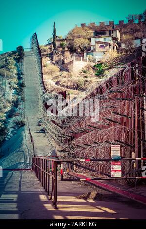 Blick auf den internationalen Grenzzaun USA/Mexiko mit Rasierdraht nach bergauf mit mexikanischen Häusern auf der anderen Seite des Zauns von Nogales, AZ, USA, Stockfoto