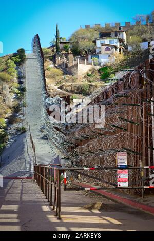 Blick auf den internationalen Grenzzaun USA/Mexiko mit Rasierdraht, der bergauf mit mexikanischen Häusern auf der anderen Seite des Zauns von Nogales, AZ, USA, in bl verläuft Stockfoto