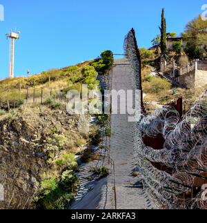 Blick auf den internationalen Metallgrenzzaun mit Stacheldraht nach dem Aufstieg zwischen Nogales, AZ, USA und Nogales, Sonora, MX, Stockfoto