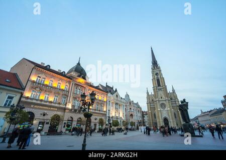 Novi SAD, SERBIEN - 26. NOVEMBER 2016: Der Name der Marienkirche, Novi Sad catholic Cathedral in der Abenddämmerung mit einer Menschenmenge, die auf dem Trg Slobode Platz spazieren geht. Das ist etwa so Stockfoto