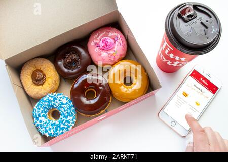 Calgary, Alberta. Kanada 27. Januar 2020. Eine Person, die ein iPhone Plus mit der Tim Hortons App verwendet, mit einem Kaffee und einer offenen Box Donuts auf einem weißen Backgr Stockfoto