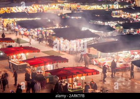 Überdachte Souq-Stände oder Essensstände in einer geschäftigen Jemaa el-Fnaa in der Abenddämmerung in Marrakesch, Marrakesch-Safi Marokko. Stockfoto