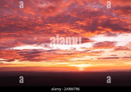 Wunderschöner Sommer Rot leuchtend brennender Sonnenuntergang oder Sonnenaufganghimmel mit Wolken und Gebirge Stockfoto