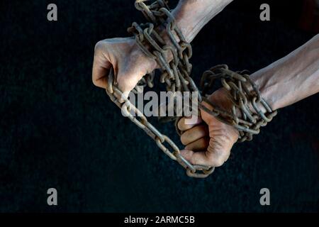 Hände eines Sklaven, der verzweifelt versucht, die Eisenkette auf einem dunklen Hintergrund zu durchbrechen, das Konzept der Gefangenen, der Menschen in der Sklaverei, die Hoffnung auf Freiheit, wenn Th Stockfoto