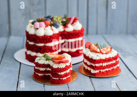 Roter, herzförmiger Kuchen mit weißen, gepeitschten cremefarbenen Scheiben frischer Erdbeeren auf grauem Hintergrund. Konzept festlicher Speisen zum Valentinstag d Stockfoto