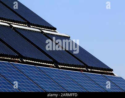 Auf dem Kombinationsdach wurden PV-Solarpaneele und die Solarwasserwärmeranlage auf braunem, geneigtem Lehmdach installiert. Sonnenkollektor Wasserleitungsheizungen Stockfoto