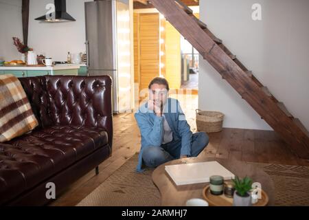 Gelangweilter Mann, der auf dem Boden in seinem Apartment sitzt Stockfoto