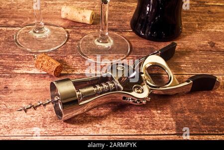 Metall-Korkenzieher auf Holzhintergrund. Flasche Rotwein, Gläser und Korken Stockfoto