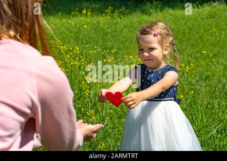 Symbol in Form eines scharlachroten Herzens. Sonniger Tag im Park. Ein Kind schenkt seiner Mutter seine Liebe. Stockfoto