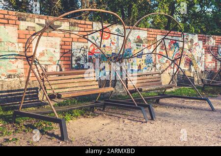 Alte Holzbank im sowjetischen Retro-Stil schwenkt im Sommer im Park in der Nähe der Mosaikwand Stockfoto