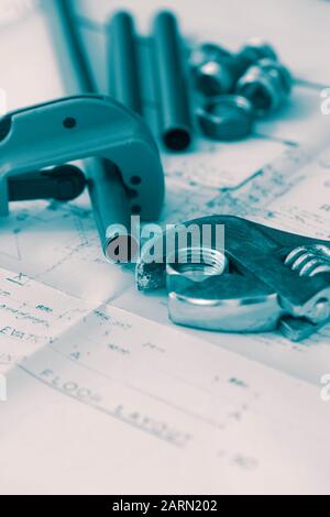Kupferrohrschneider und verstellbare Schraubenschlüsselwerkzeuge auf einer Reihe von Architektur-Bauplänen mit Rohrleitungsanschlüssen. Blaue Verlaufsfarbe Stockfoto