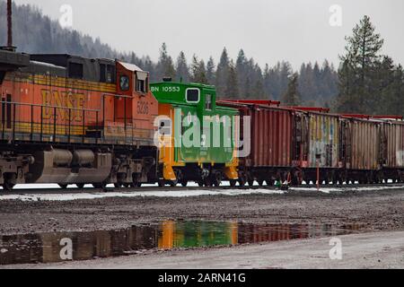 Eine Burlington Northern BNSF Railroad caboose und eine Linie von Kastenwagen hinter einer BNSF-Diesellokomotive, auf den Gleisen in der Stadt Troy, Montana. Stockfoto