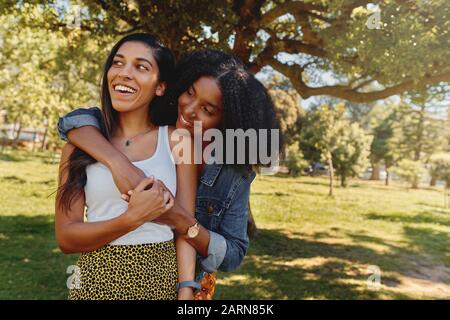 Die junge afroamerikanische Frau umarmt ihren Freund, der im Park Liebe und Fürsorge zeigt - zwei schöne Frauen, die draußen umarmen Stockfoto