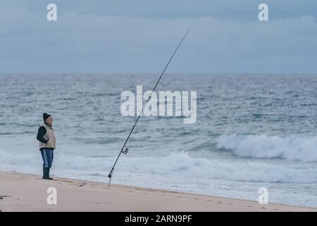 Tavira, Portugal - 23. Januar 2020: Ein einsamer Thunfischer wirft seine Linie ins Meer und wartet bei kaltem Winterwetter auf einen Biss Stockfoto