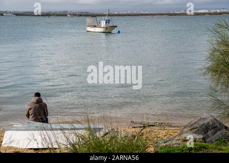 Isla Cristina, Spanien - 23. Januar 2020: Junger Mann sitzt am Strand und beobachtet Boote im Marschland Stockfoto