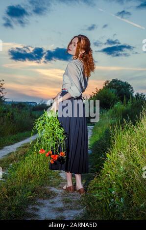 Schöne braungebrannte Mädchen in weißen besticktes Kleid Holding in den Händen Blumenstrauß der ährchen. Glücklich lächelnde Frau Spaß haben, Wandern auf dem Feld. Konzept Stockfoto