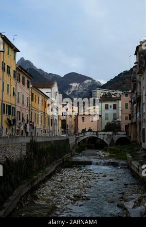 Fluss, der durch Carrara, Toskana, Italien unter einer Bogenbrücke zwischen bunten historischen Häusern fließt Stockfoto