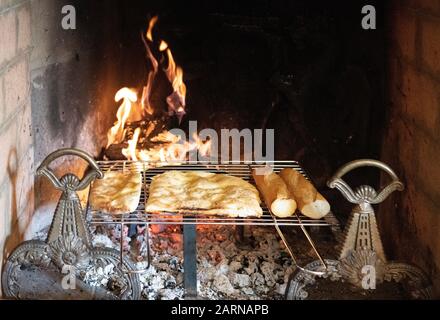 Brotheizung auf einem Regal über heißen Kohlen in einem Ziegelkamin mit brennendem Feuer in Nahaufnahme Stockfoto