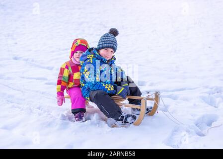 Mädchen und Junge auf Schlitten. Bruder und Schwester im Winter Kleidung mit Jacke, Kappe und Handschuhen. Stockfoto