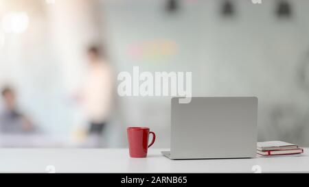 Nahaufnahme des einfachen Arbeitsbereichs mit Laptop, Notebooks, roter Kaffeetasse und Kopierbereich auf weißem Schreibtisch mit verschwommenem Hintergrund im Bürozimmer Stockfoto