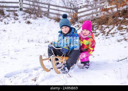 Der Junge und das Mädchen machen sich bereit, auf einem Schlitten von der Spitze des Hügels herabzukommen. Winterzeit Stockfoto