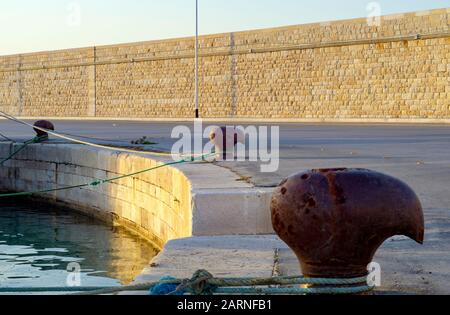 Metall-Liegeplatz an der Anlegestelle des Betonhafen-Piers, gegen Küstenstadt, selektive Konzentration auf Bollard. Stockfoto