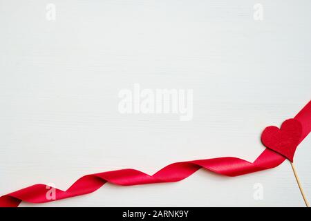 Rotes Band mit einem Herzen aus Stoff auf weißem Holzhintergrund. Draufsicht. Stockfoto
