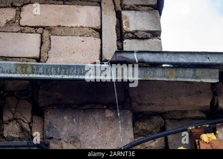 Metallisches Regenwasser fließt an der Ziegelwand ab Stockfoto