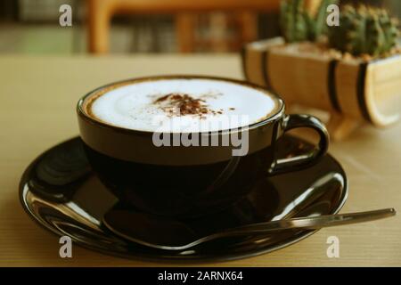 Cappuccino-Kaffee in einer schwarzen Tasse auf Holztisch Stockfoto